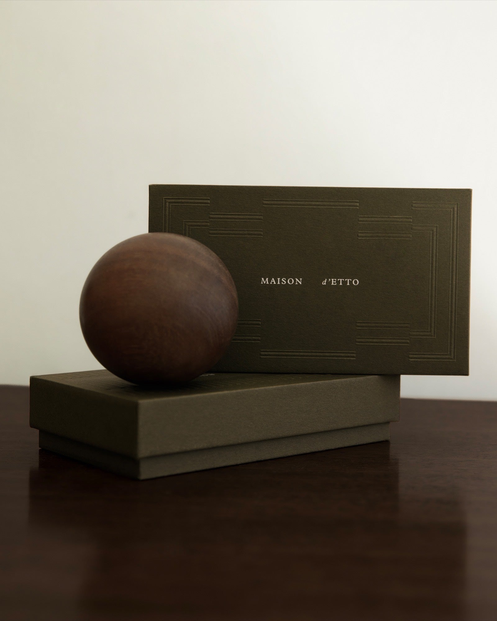 A Maison d'Etto box and a turned wooden sphere on a dark table